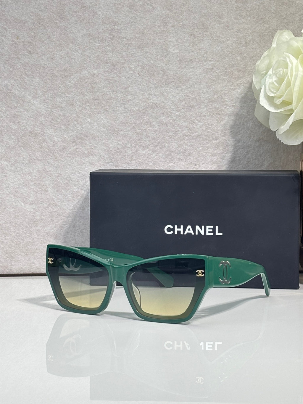 Eyeglasses with green square frames and tinted lenses, CHANEL logo on temples.