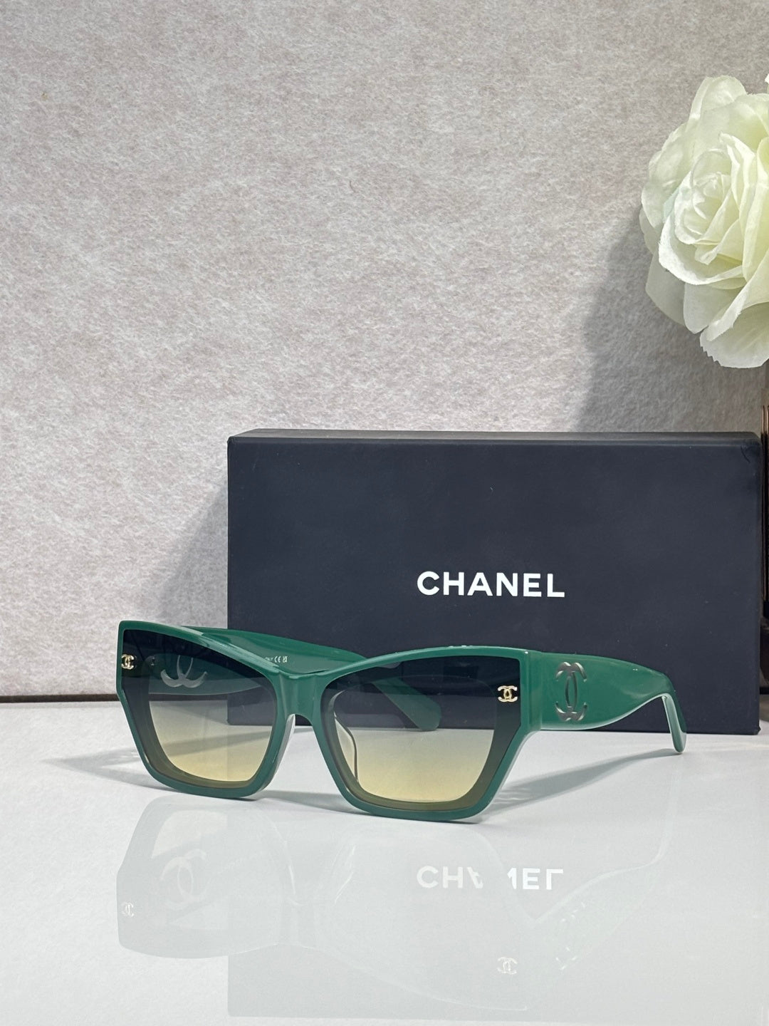 Eyeglasses with green square frames and tinted lenses, CHANEL logo on temples.