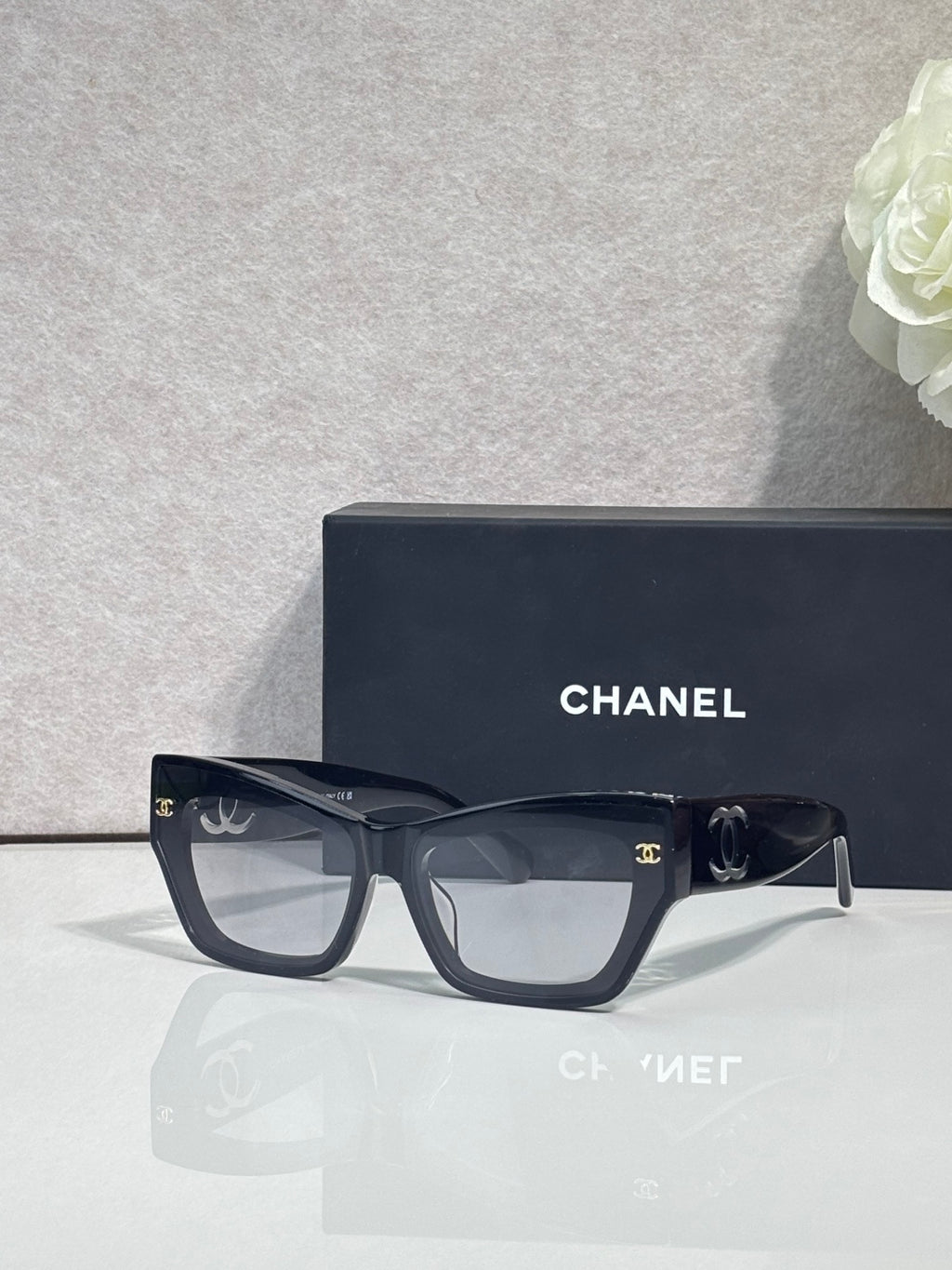 Eyeglasses with black square frames and tinted lenses, CHANEL logo on temples.