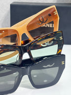 Close-up of layered CHANEL eyeglass frames: amber and dark square styles with logo.