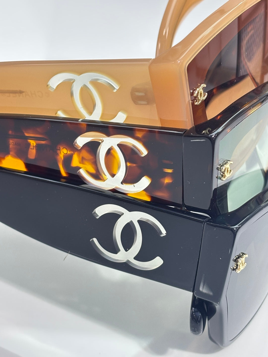 Close-up of CHANEL eyeglass frames in amber and dark with metal logo hardware.