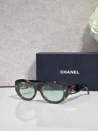 Dark tortoise round-frame Chanel eyeglasses with logo temples and tinted lenses.
