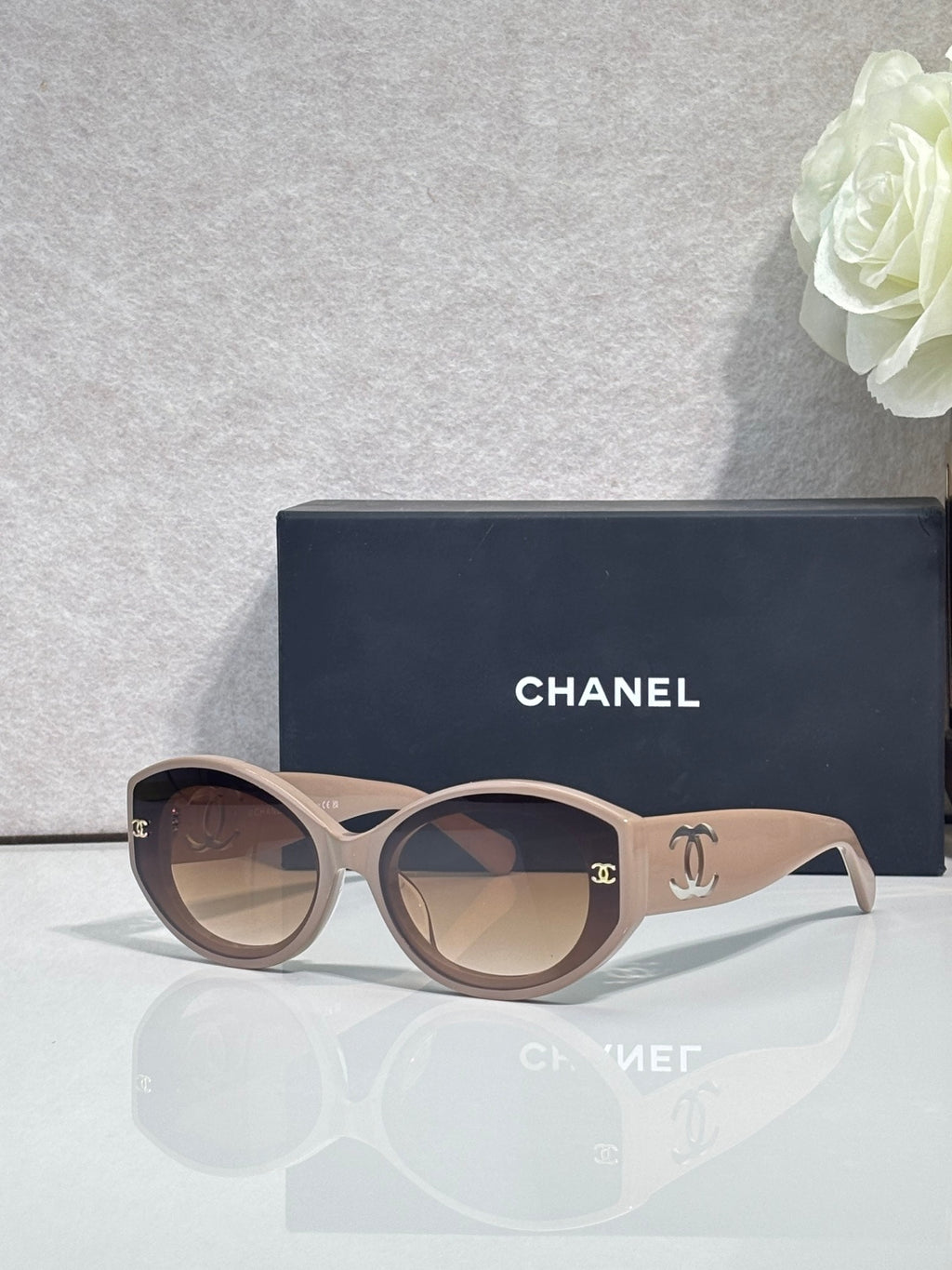 Beige round-frame Chanel eyeglasses with logo temples and dark lenses.