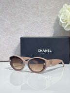 Beige round-frame Chanel eyeglasses with logo temples and dark lenses.