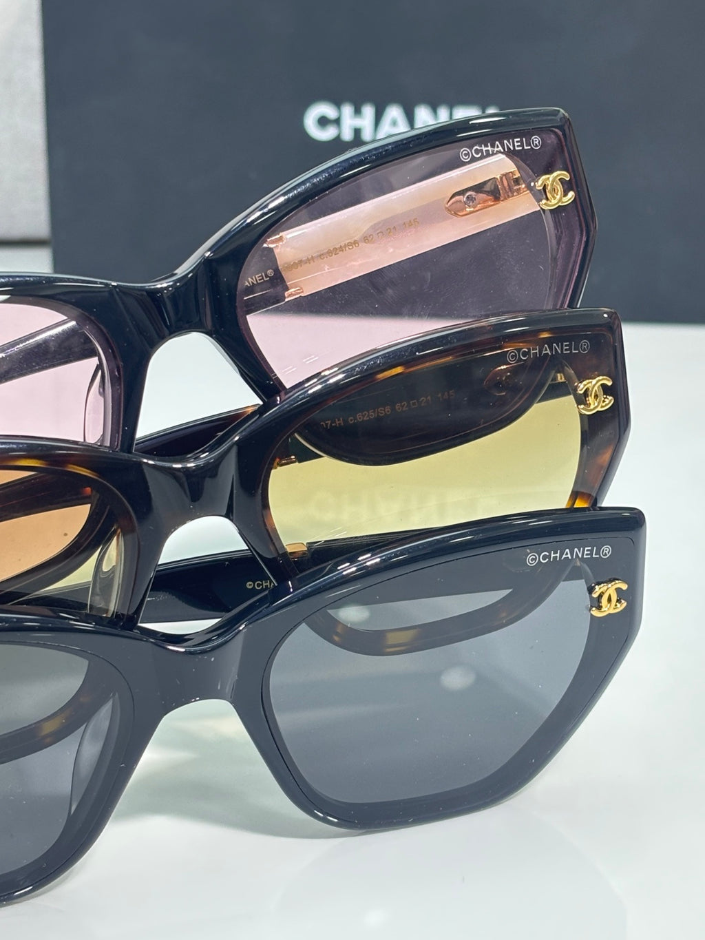 Chanel glasses close-up with glossy dark frames, reflective lenses, gold CC logo hardware