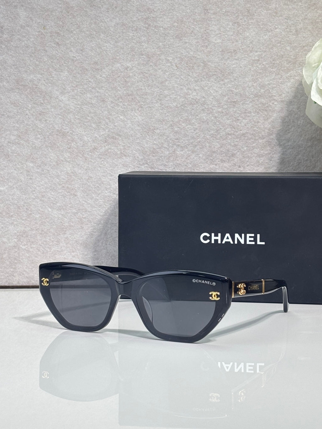 Chanel glasses with dark blue-black frames and smoky lenses, gold CC emblem at temples