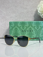 Gold-tone sunglasses with dark lenses and green patterned side arms