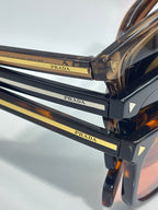 Prada sunglasses frame closeup with gold branding and tortoise-brown temple tips