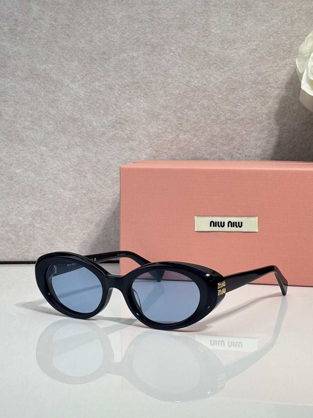 MiuMiu black oval sunglasses with blue lenses and Miu Miu logo at temple