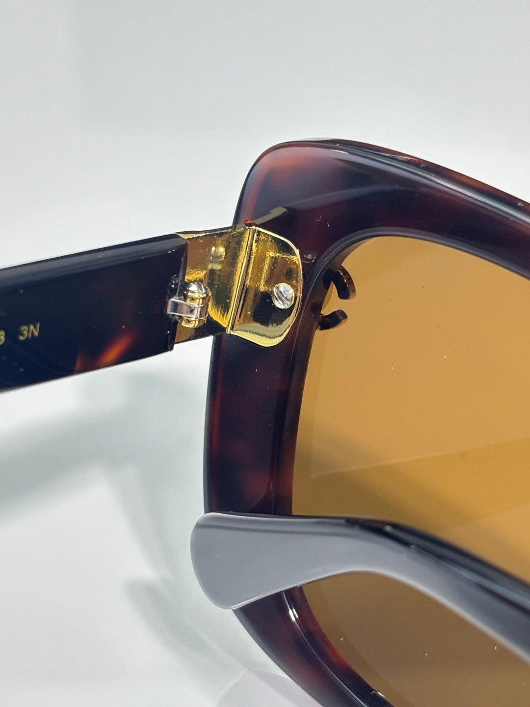 Chanel sunglasses close-up: tortoiseshell frame with gold hinge and amber lenses