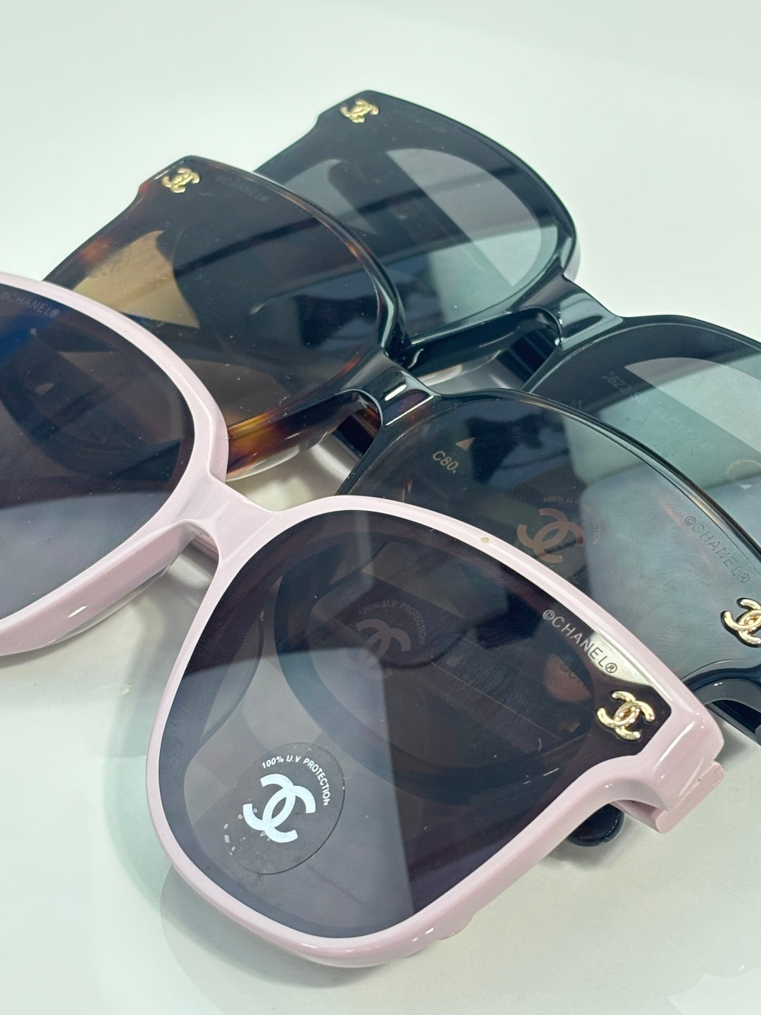 Chanel sunglasses angled on display with pink and navy frames and dark tinted lenses.