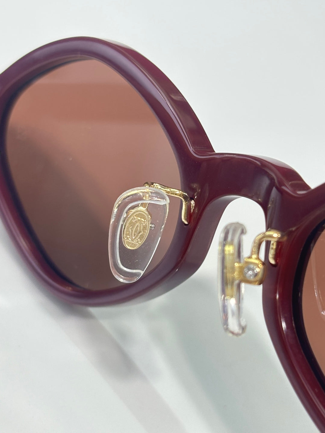 Close-up burgundy round eyeglasses with gold emblem on the temple