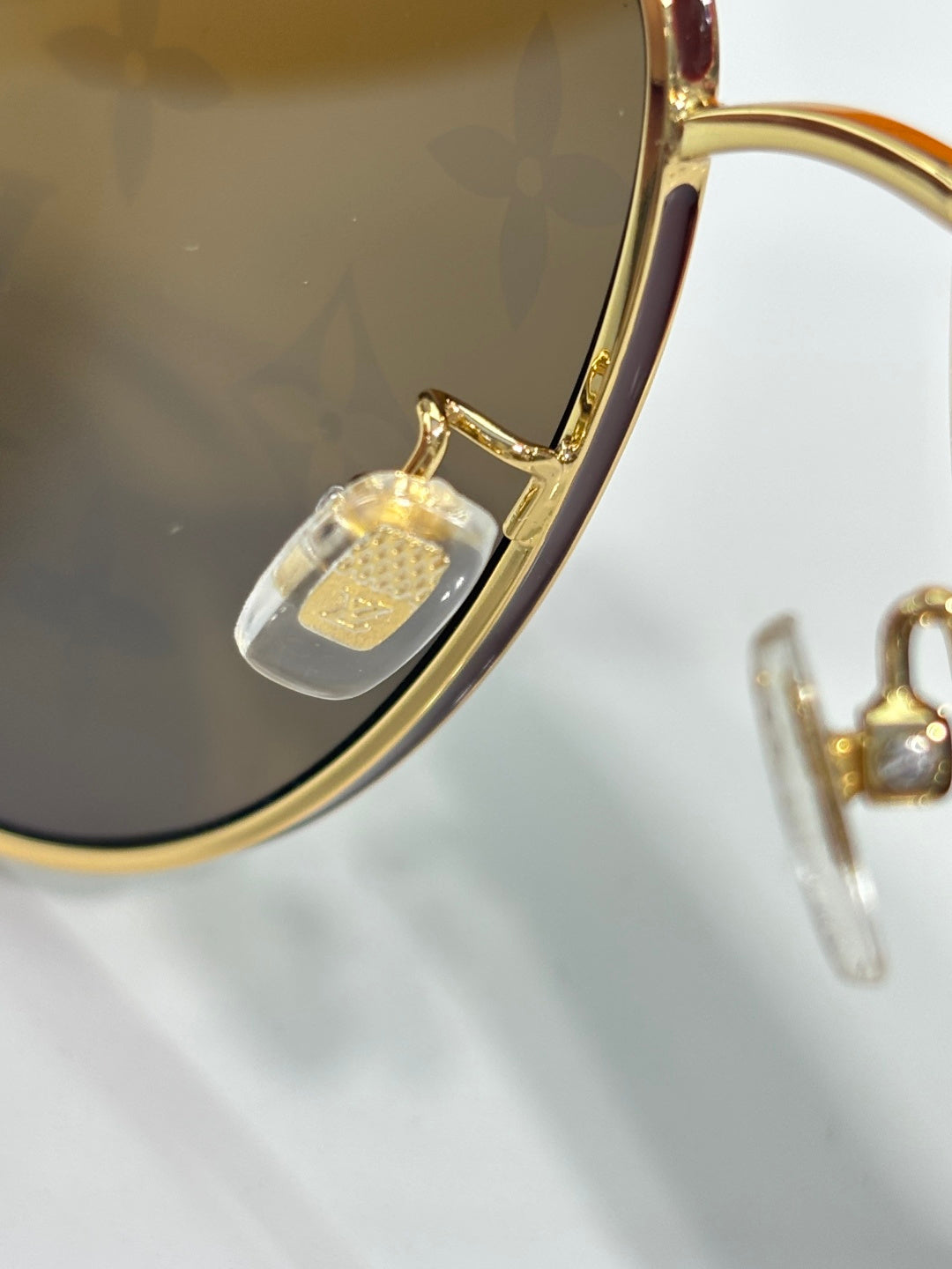 Louis Vuitton sunglasses close-up: dark lens with gold-tone curved frame and temple detail.