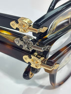 Eyeglasses temple close-up with gold hinge plates and engraved floral accents