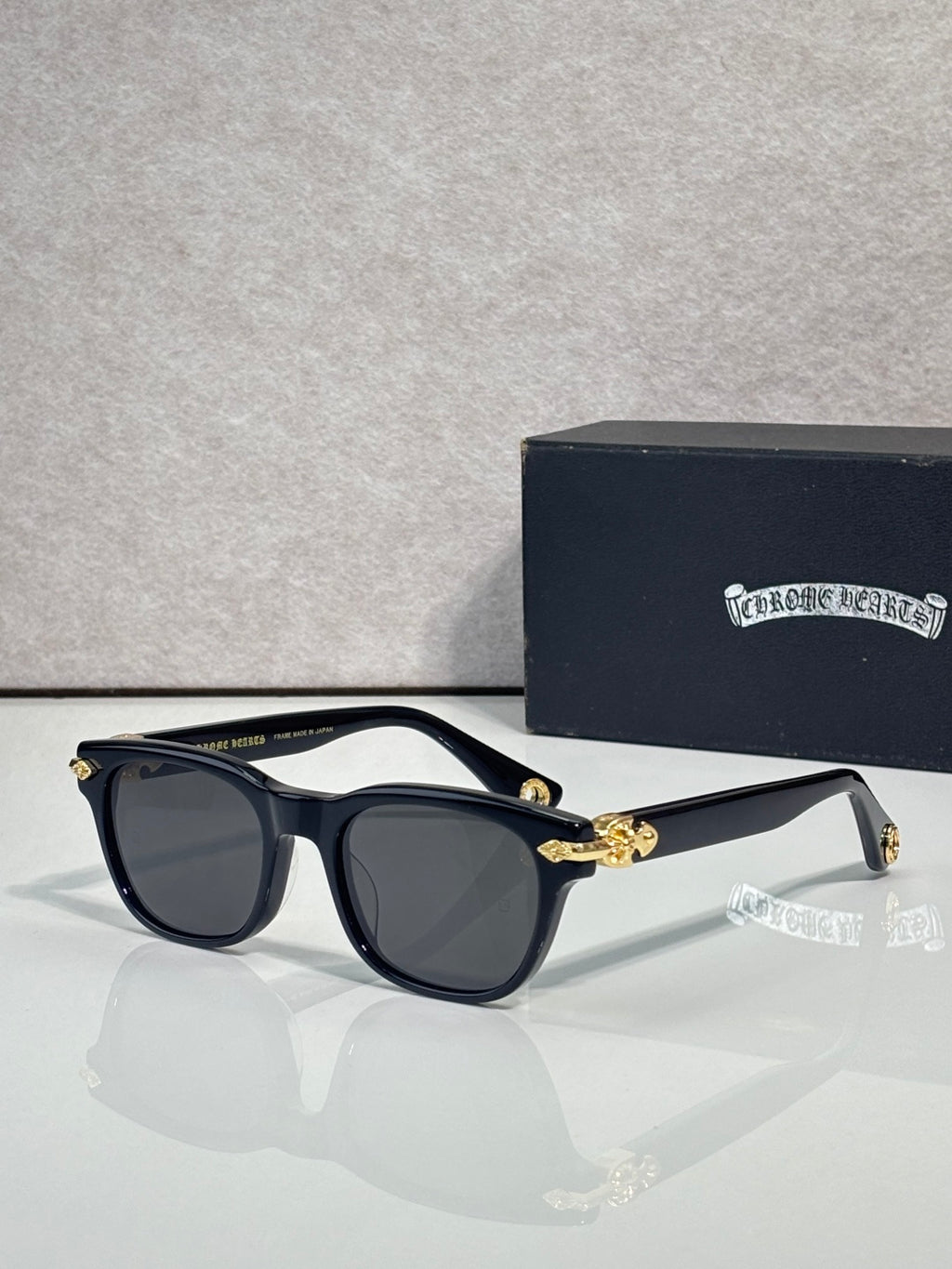 Dark blue sunglasses with gray lenses and gold-tone bow detail at the temples