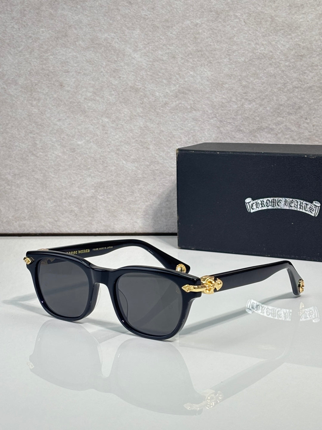 Dark blue sunglasses with gray lenses and gold-tone bow detail at the temples