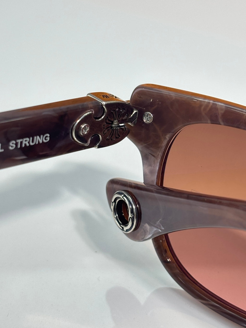 Brown sunglasses with engraved metal emblem on the temple near the hinge