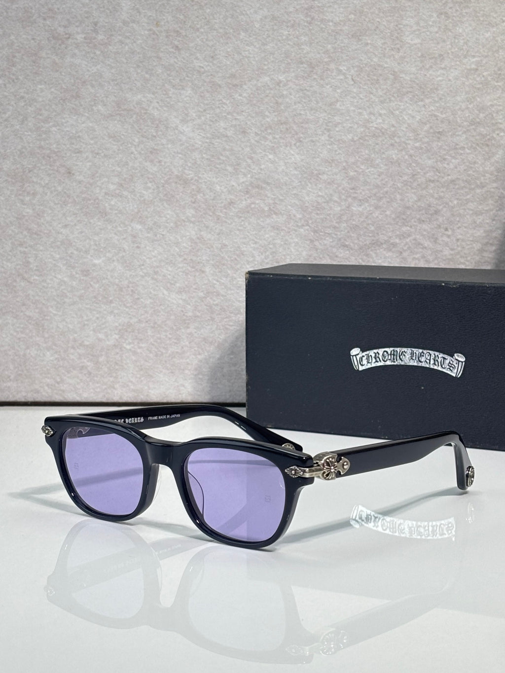 Purple-tinted sunglasses with dark blue frame and gold-tone temple accents