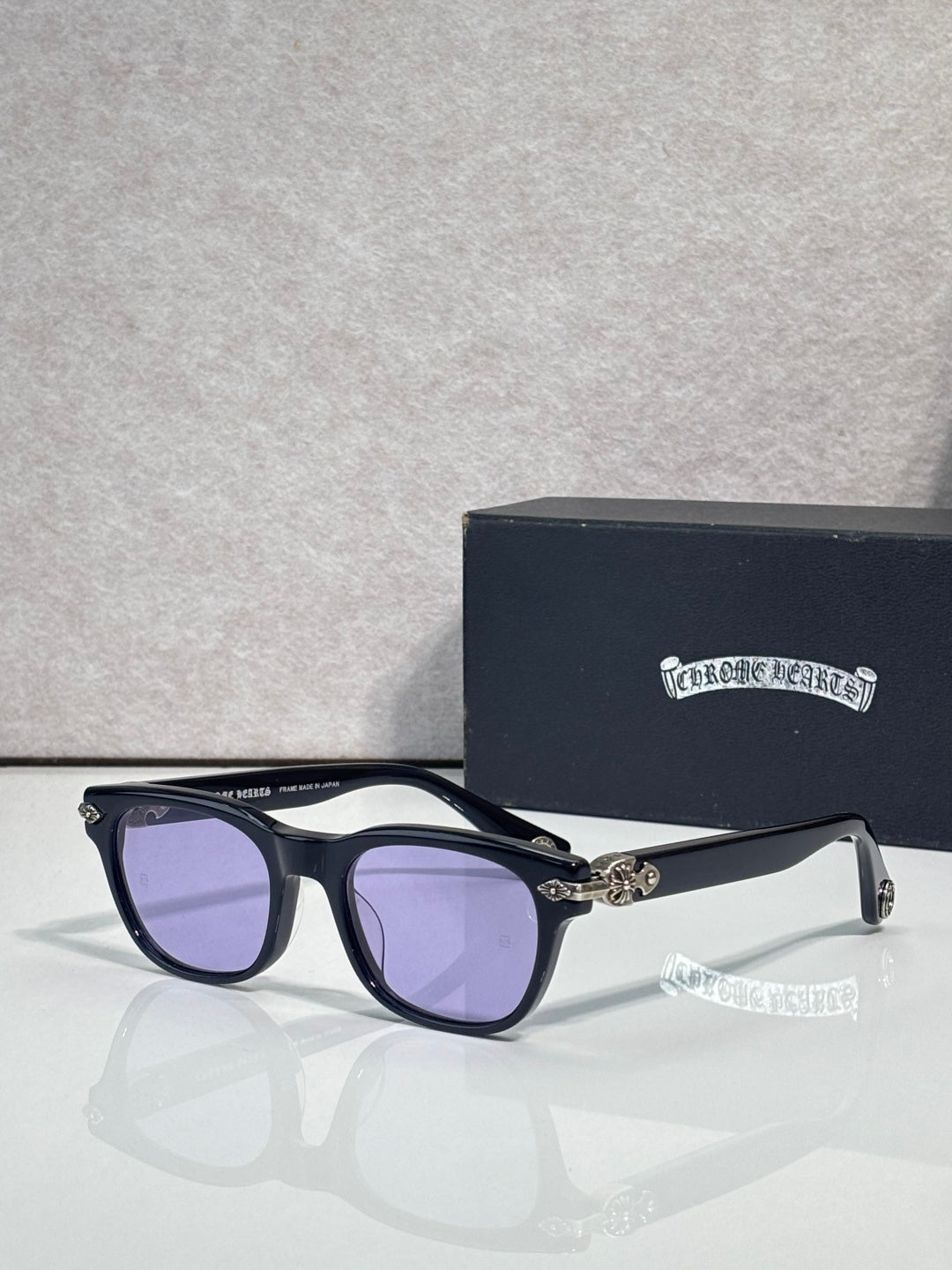 Purple-tinted sunglasses with dark blue frame and gold-tone temple accents