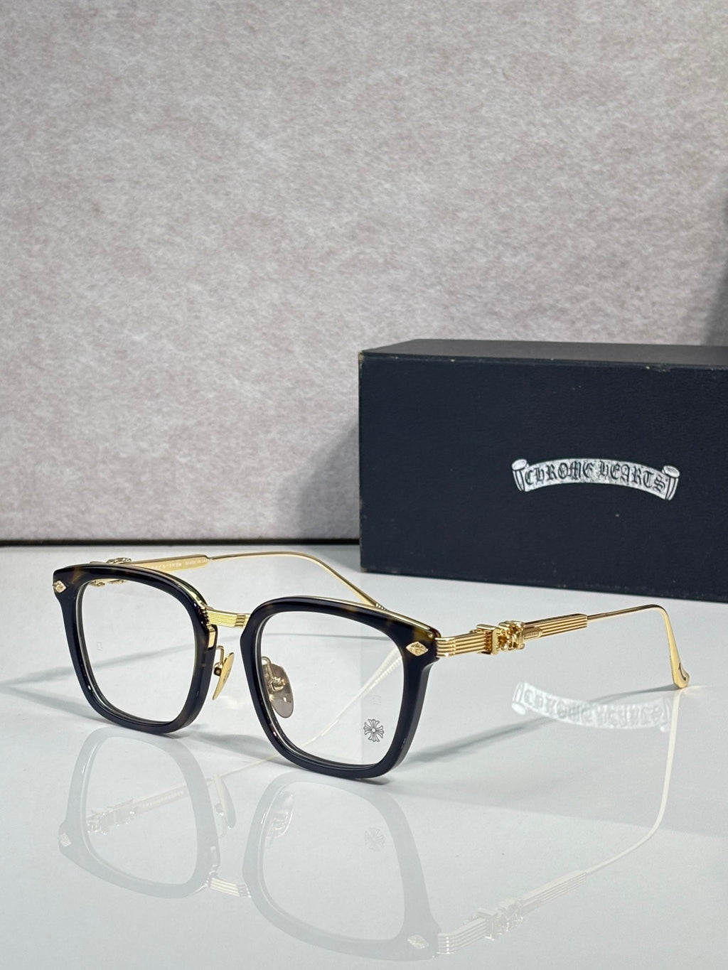 Gold eyeglasses with rectangular clear lenses, dark blue inner frame, and gold temples