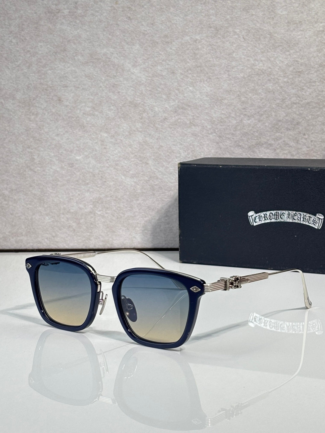 Square sunglasses with light amber lenses, dark blue frame, gold temple accents, chrome trim