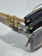 Chrome glasses close-up: gold temple hinge and ridged metal detailing on dark frame