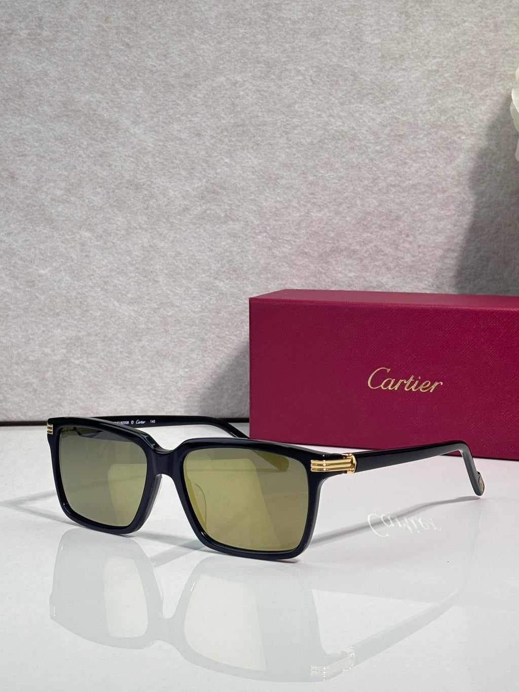 Black square sunglasses with green-tinted lenses and gold-tone bar at the bridge