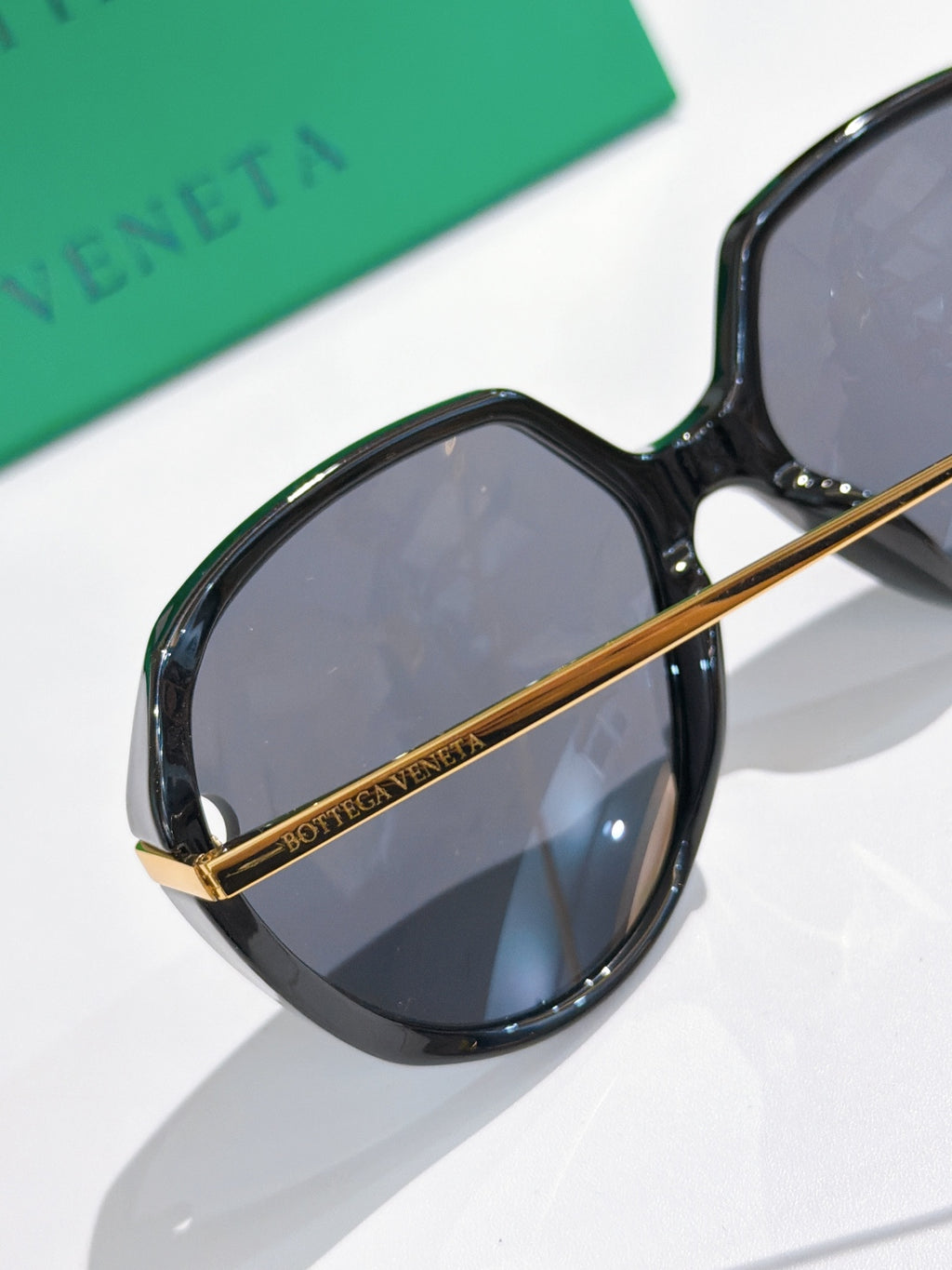 Bottega Veneta oval sunglasses, black frames with gold hinge and tinted blue lenses.