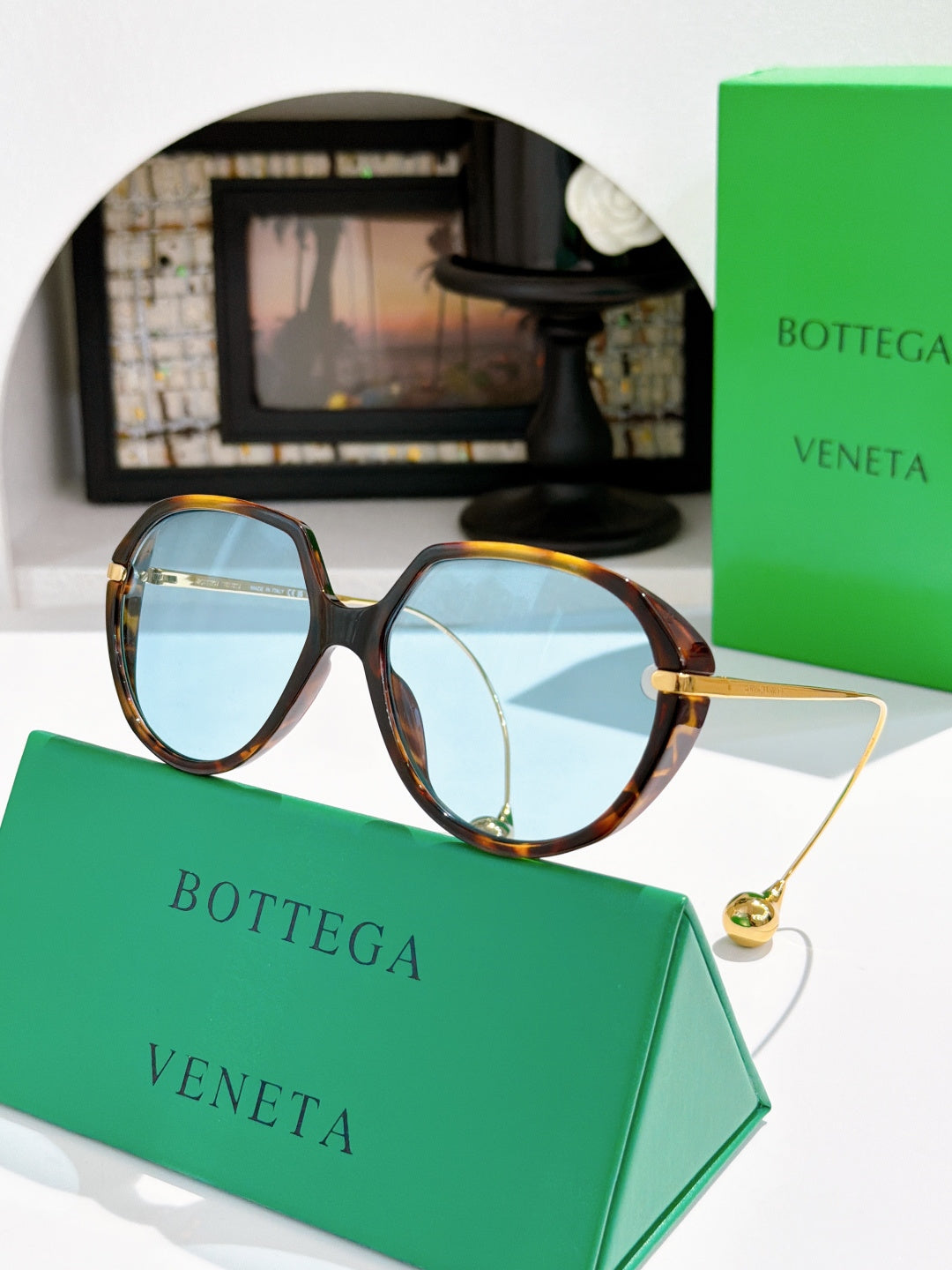 Bottega Veneta sunglasses with dark tortoise frame and light blue lenses, gold arm tips.