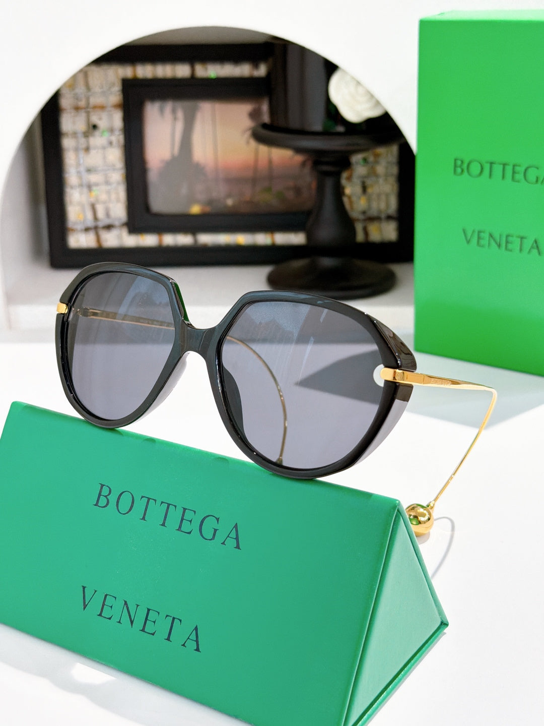 Bottega Veneta sunglasses with black frame and smoky gray lenses, gold arm detail.