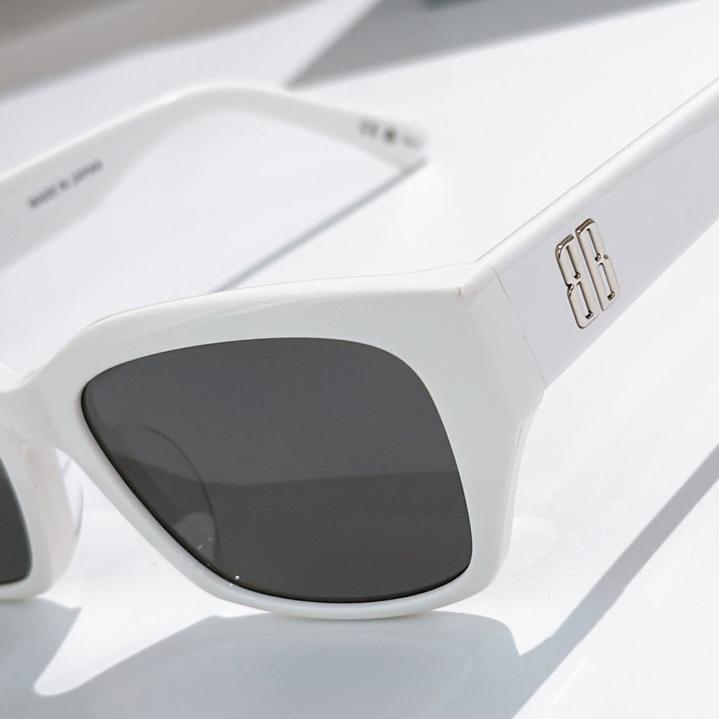 Balenciaga white sunglasses close-up with dark tinted lenses and metallic temple logo