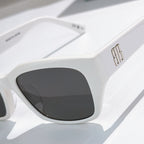 Balenciaga white sunglasses close-up with dark tinted lenses and metallic temple logo