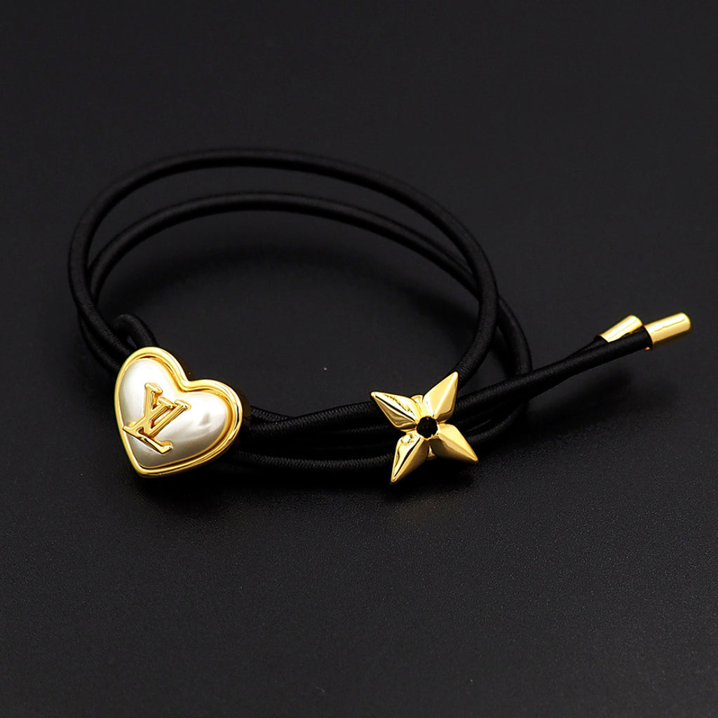 Black cord bracelet with gold heart charm and gold star accent on dark background
