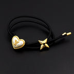 Black cord bracelet with gold heart charm and gold star accent on dark background