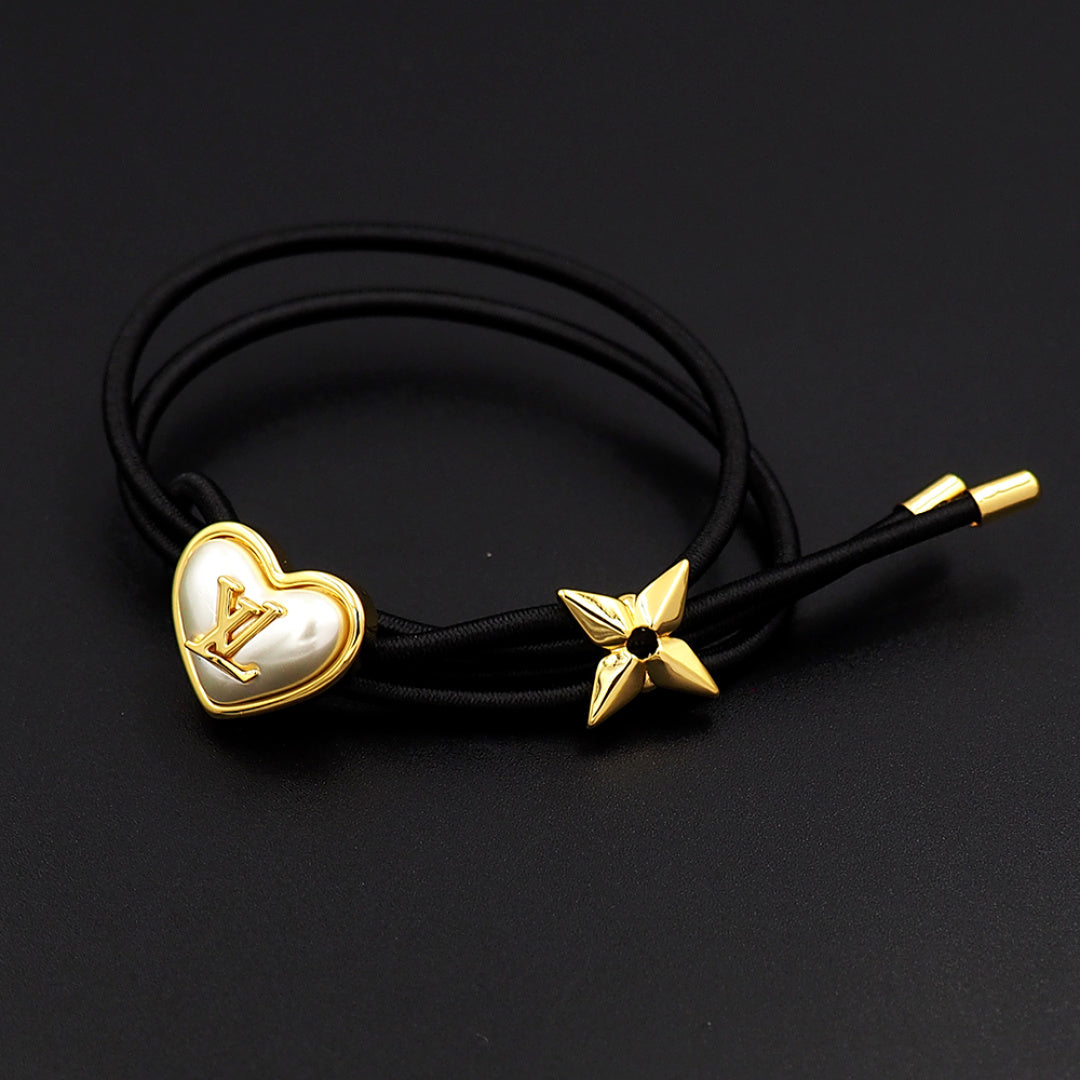 Black cord bracelet with gold heart charm and gold star accent on dark background