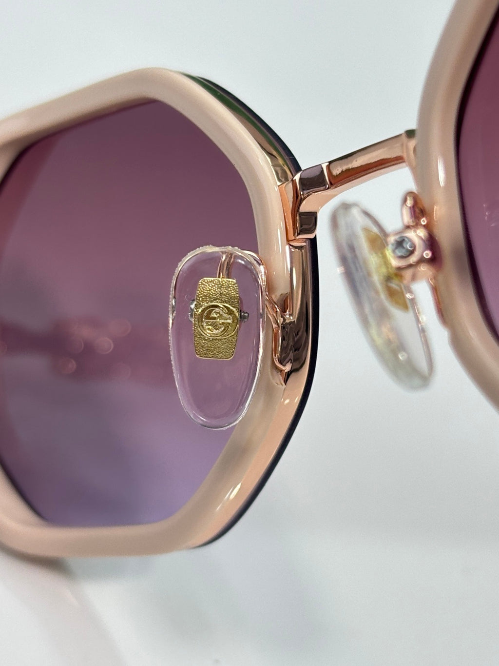 Gucci sunglasses close-up, round purple lens, gold-tone frame with small logo charm.
