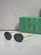 Gucci sunglasses, round dark lenses, gold-tone frame with chain detail on temples.
