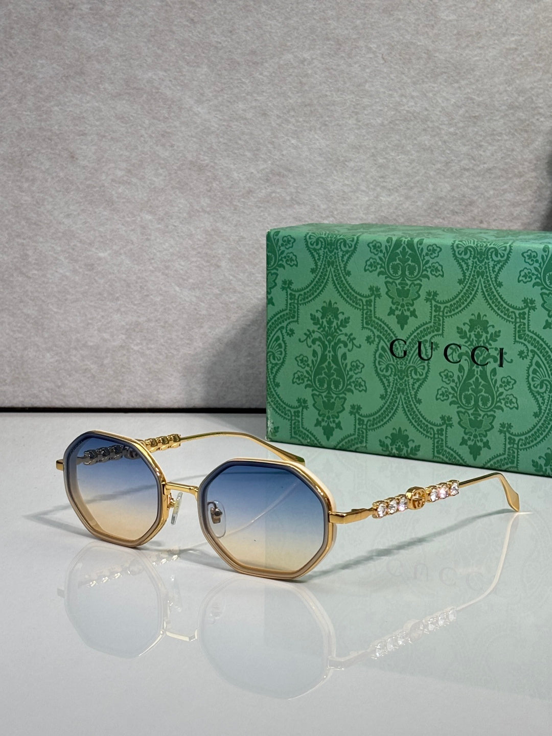 Gucci sunglasses, round blue gradient lenses, gold-tone frame with chain detail on temples.