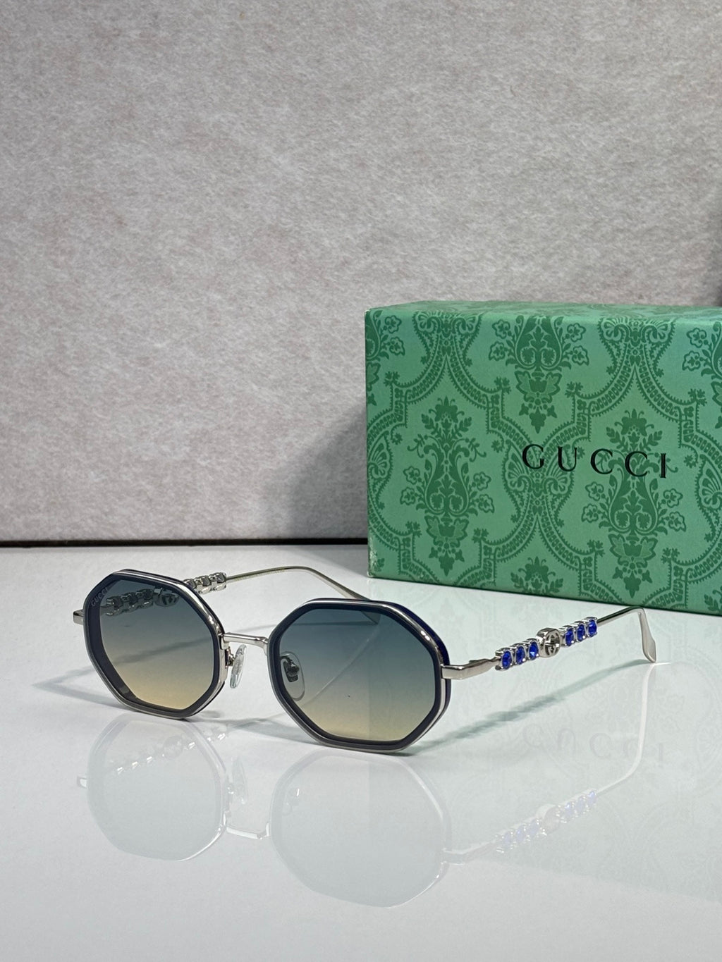 Gucci sunglasses, round blue gradient lenses, silver-tone frame with jeweled temple detail.