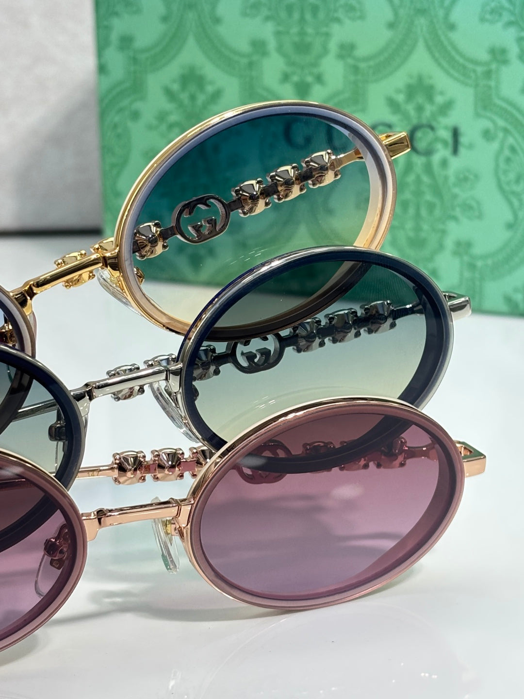 Gucci round sunglasses close-up with dark, green-tinted, and purple lenses; gold and silver frames.