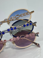 Gucci round sunglasses close-up with jeweled arms and blue, pink, and dark lenses.