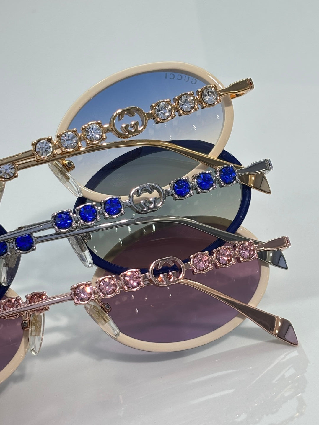 Gucci round sunglasses close-up with jeweled arms and blue, pink, and dark lenses.