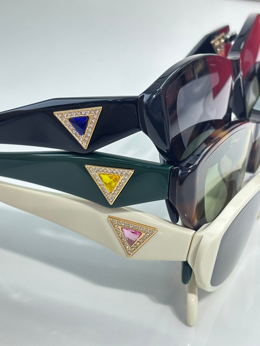 Close-up of dark green and black cat-eye sunglasses with gold triangular emblem details