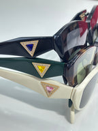 Close-up of dark green and black cat-eye sunglasses with gold triangular emblem details