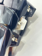 Prada sunglasses detail of metal hinge and black temple with triangular emblem.