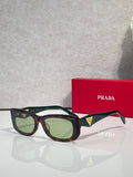 Prada sunglasses with dark frames and green-tinted lenses, triangular logo on temple.