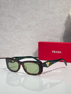 Prada sunglasses with dark frames and green-tinted lenses, triangular logo on temple.