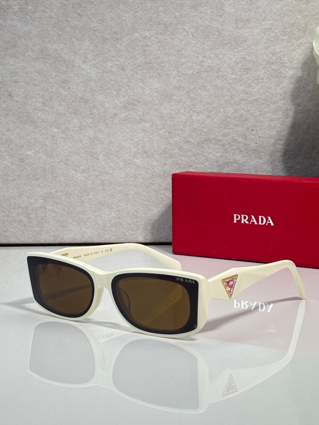 Prada sunglasses with white frames and brown-tinted lenses, triangular logo on temple.