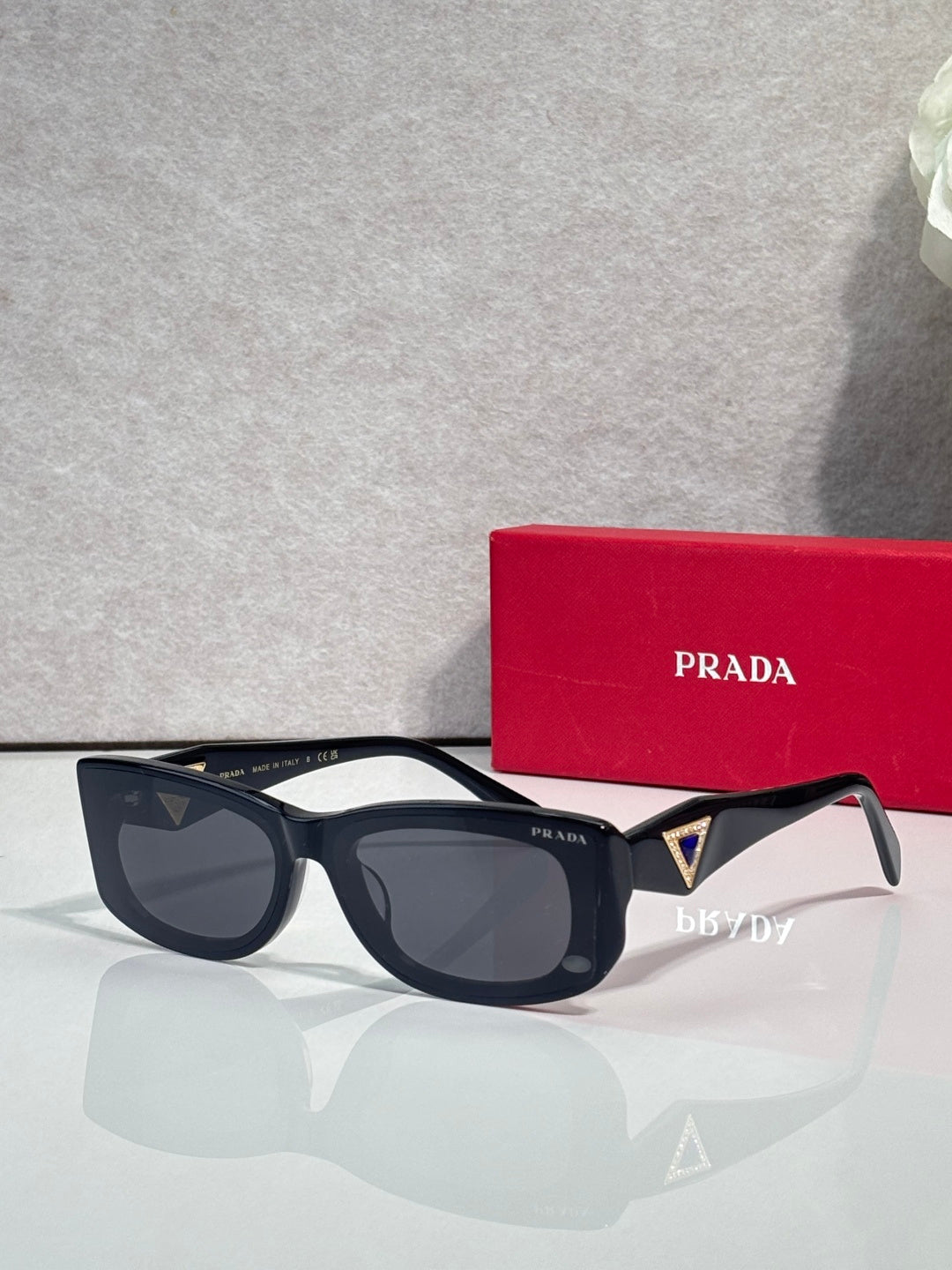 Prada sunglasses with black frames and dark lenses, triangular logo on side arm.