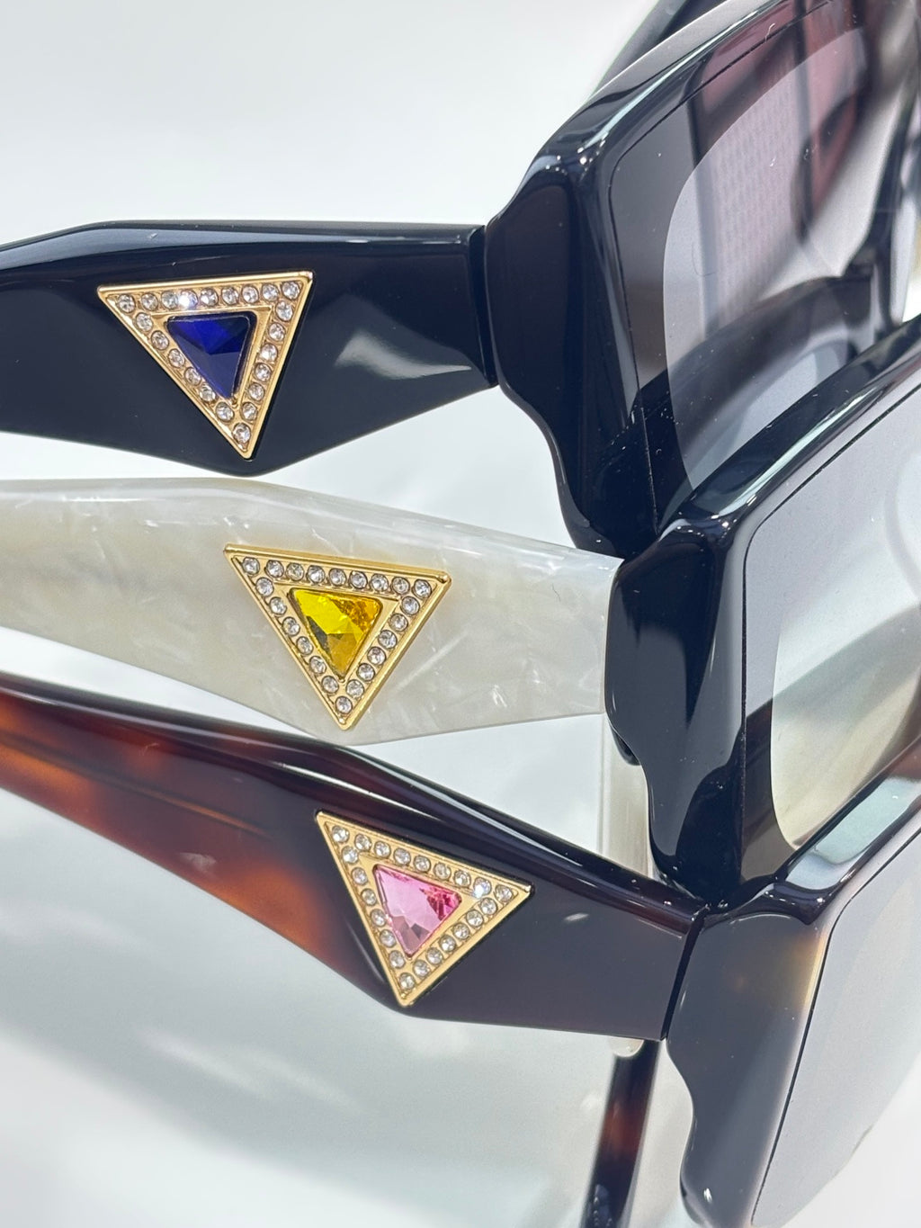 Prada sunglasses close-up of triangular jeweled logo on dark temple arm.